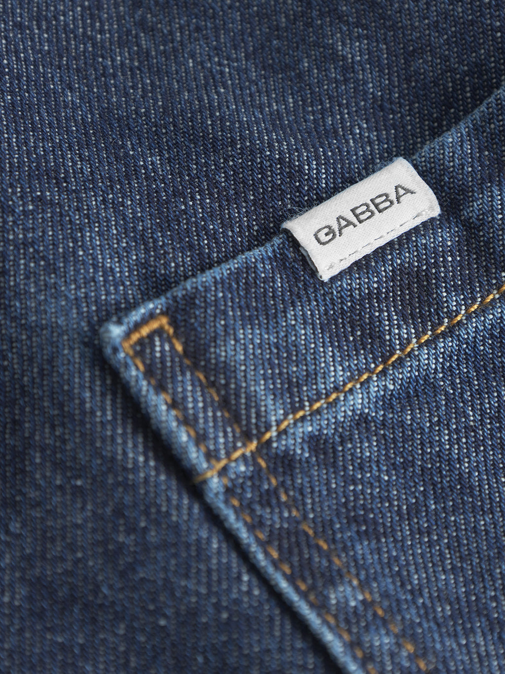Close-up of mid blue denim with visible stitching and a small white Gabba label. The texture and weave evoke classic workwear, showcasing quality and detail. A perfect example of craftsmanship in the Ugo Cargo Fone Denim Shorts.