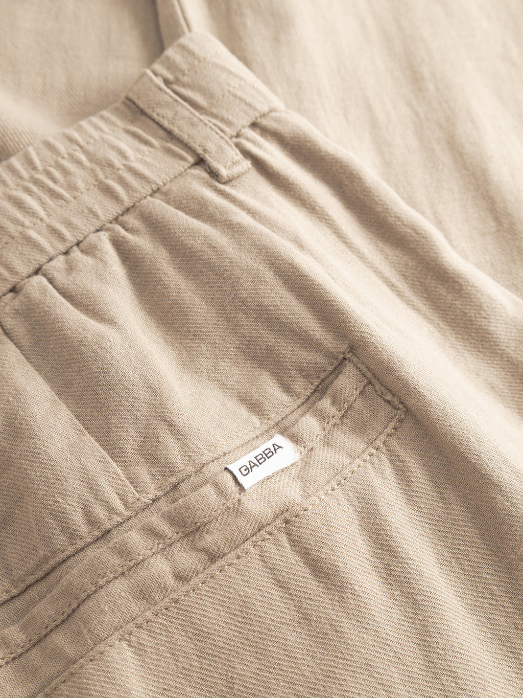 Close-up of Gabba Monza Lino Cropped - Sand Plaza pants, highlighting the back pocket, elastic waistband, and small white Gabba label. Soft, lightweight fabric offers comfort with a relaxed fit.