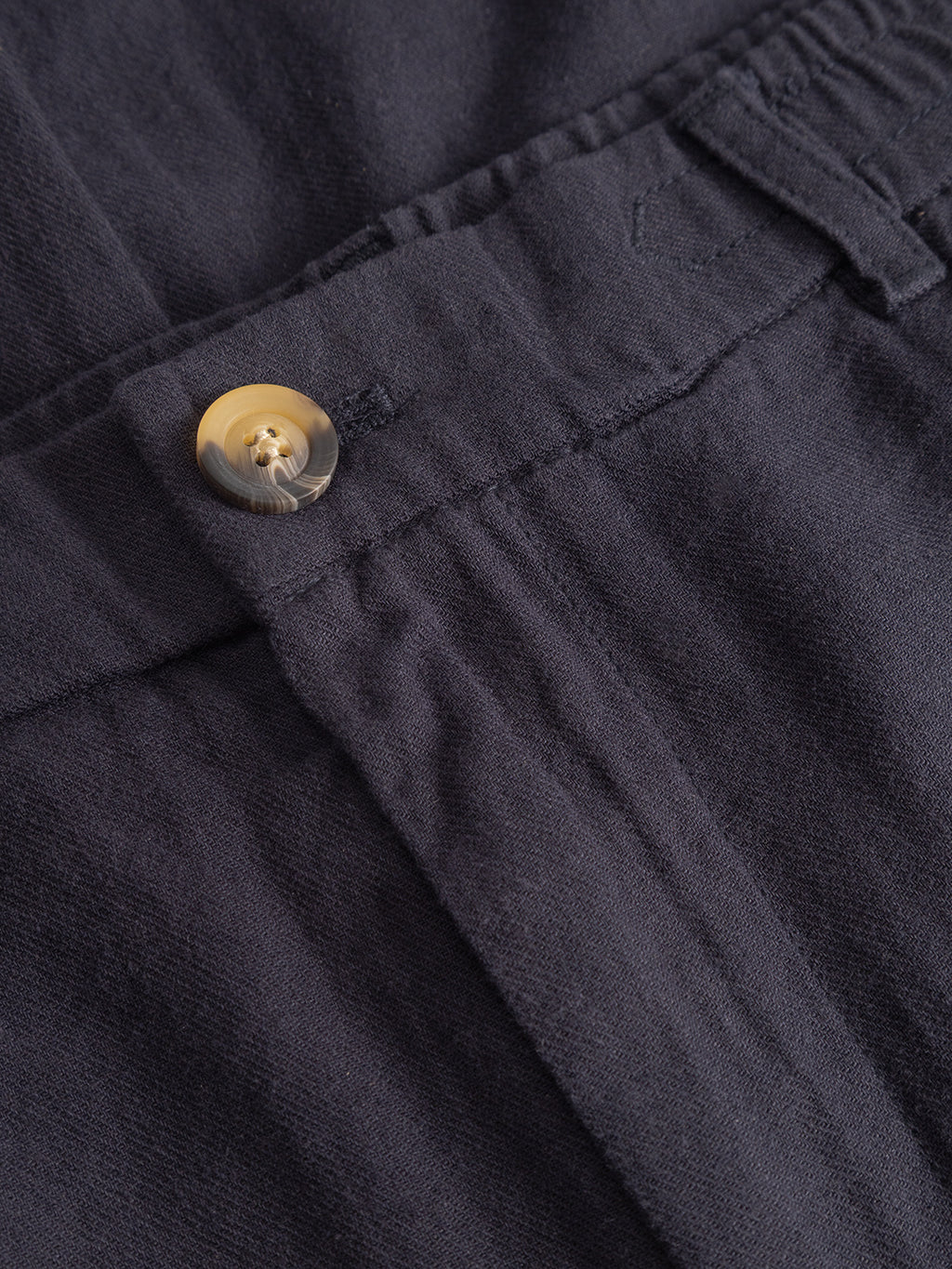 Close-up of the Monza Lino Cropped - Night Sky by Gabba, showing a dark navy elastic waistband with a light brown button and visible stitching on soft, textured fabric—ideal for comfortable, straight-fit pants.