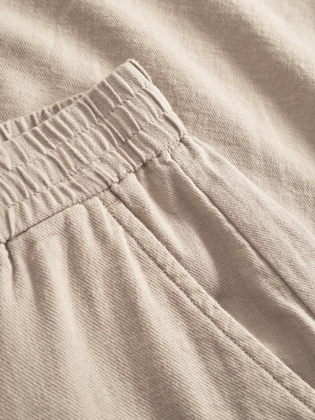 Close-up of Alfa Lino - Sand Plaza fabric pants by Gabba, featuring an elastic waistband and neatly stitched pocket. The linen-like texture appears soft and slightly textured, epitomizing casual style with superior comfort.
