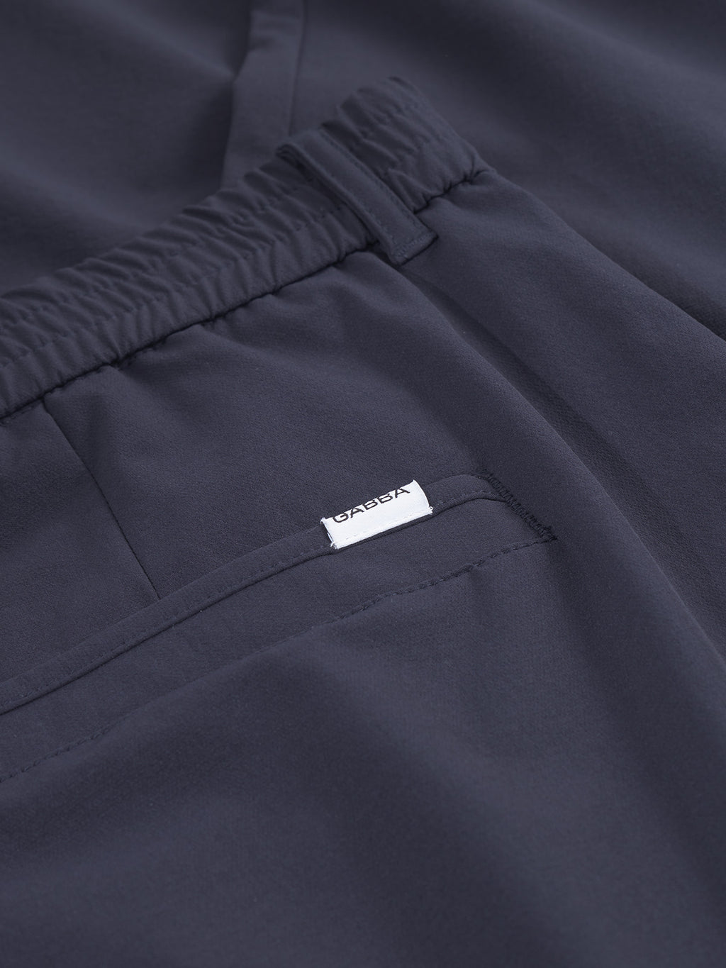 Close-up of navy Monza Tech pants by Gabba, showcasing an elastic waist and a pocket with a small white Gabba label. The tech fabric is smooth and slightly textured, providing a relaxed straight fit for comfort and style.