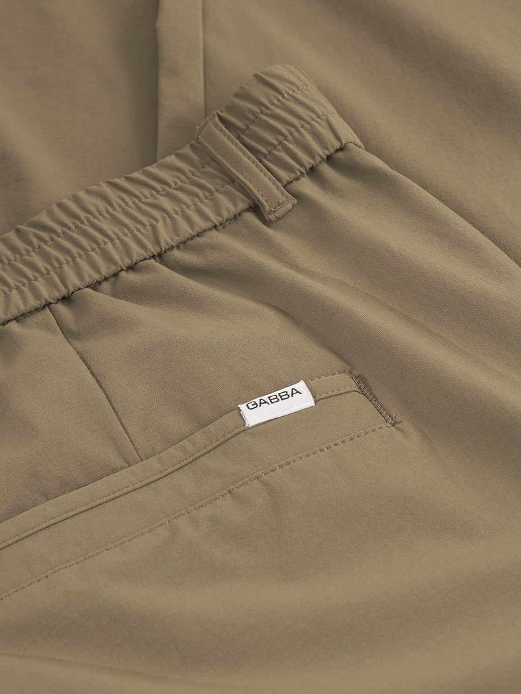 Close-up of Gabbas Monza Tech - Army pants in khaki, showcasing an elastic waistband and a back pocket with a white GABBA label. Made from lightweight tech fabric, these pants blend comfort with style.