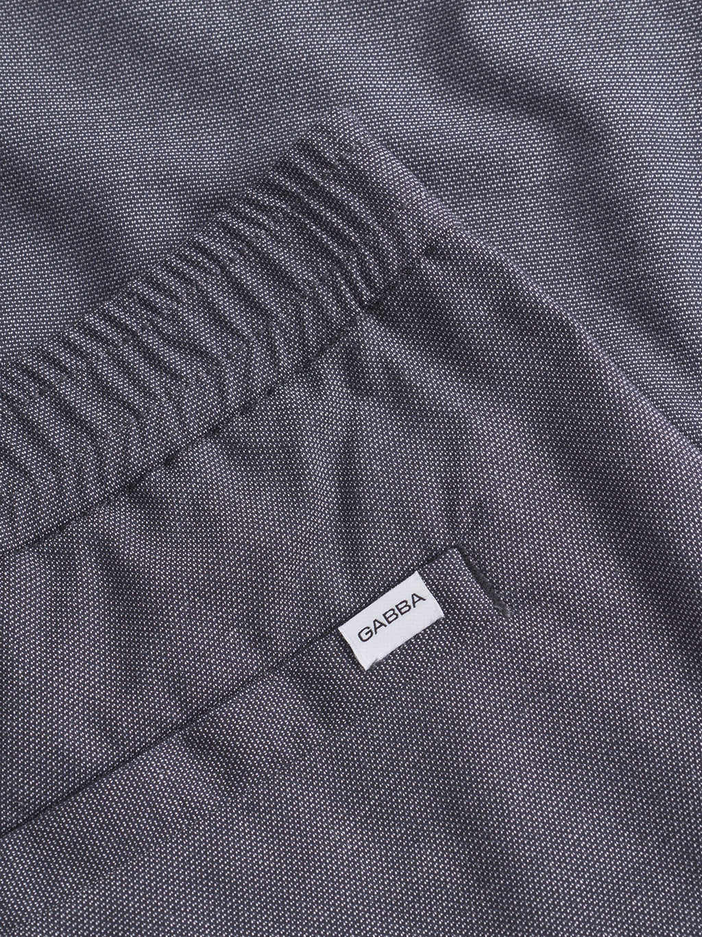 A close-up of a dark gray textured fabric with a small white Gabba label near a pocket. The Napoli 19 Carre - Navy pants design features a subtle dotted pattern and neatly stitched edges on the pocket for added comfort.