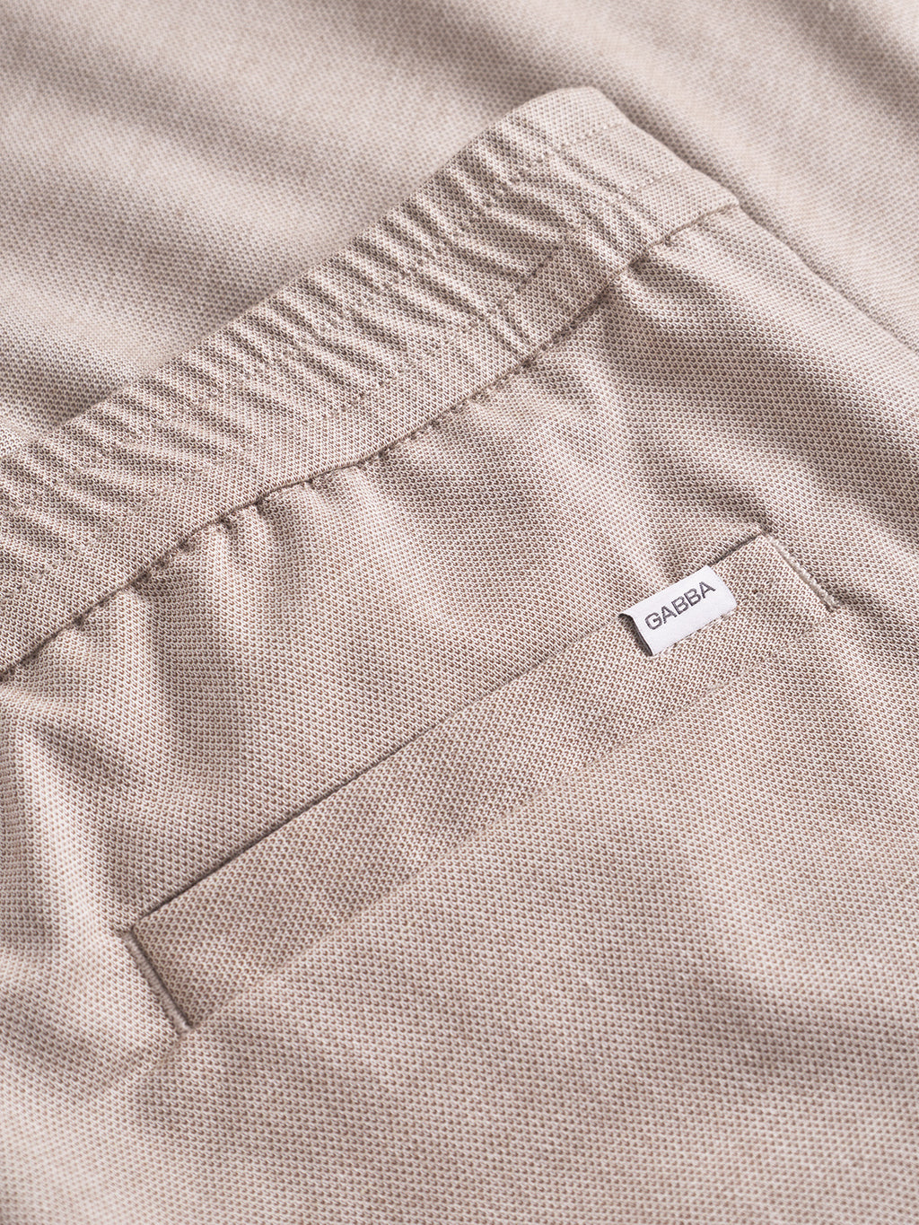Close-up of the beige fabric shows a back pocket with a small white Gabba label on the seam. The Napoli 19 Carre - Sand pants have a textured, speckled look and an elastic waistband for comfort.