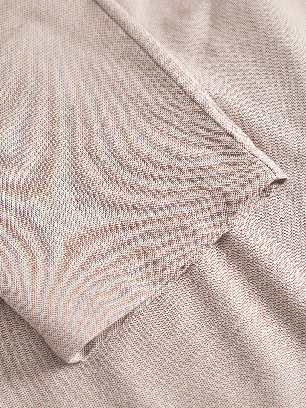 Close-up of Gabbas Napoli 19 Carre - Sand fabric, showcasing its light beige hue and subtle dotted pattern. The focus is on the comforting texture reminiscent of classic pants, with a folded edge highlighting its fine stitching.
