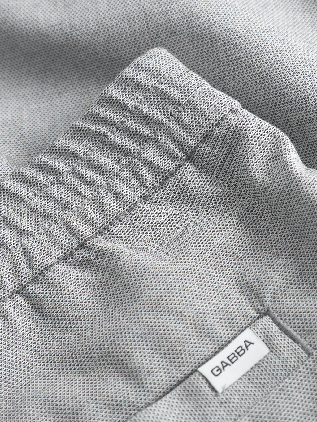 Close-up of light grey textured fabric with a visible elastic waistband, offering unmatched comfort. A small white tag labeled Gabba is sewn onto the classic Napoli 19 Carre pants.