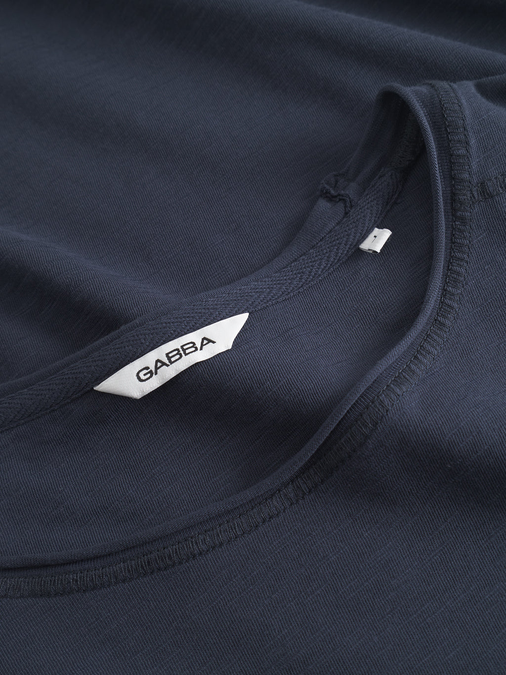A close-up of the Gabba Kostant New SS - Navy T-shirt showcases its slub fabric’s unique texture and detailed stitching, with a white Gabba label near the collar.