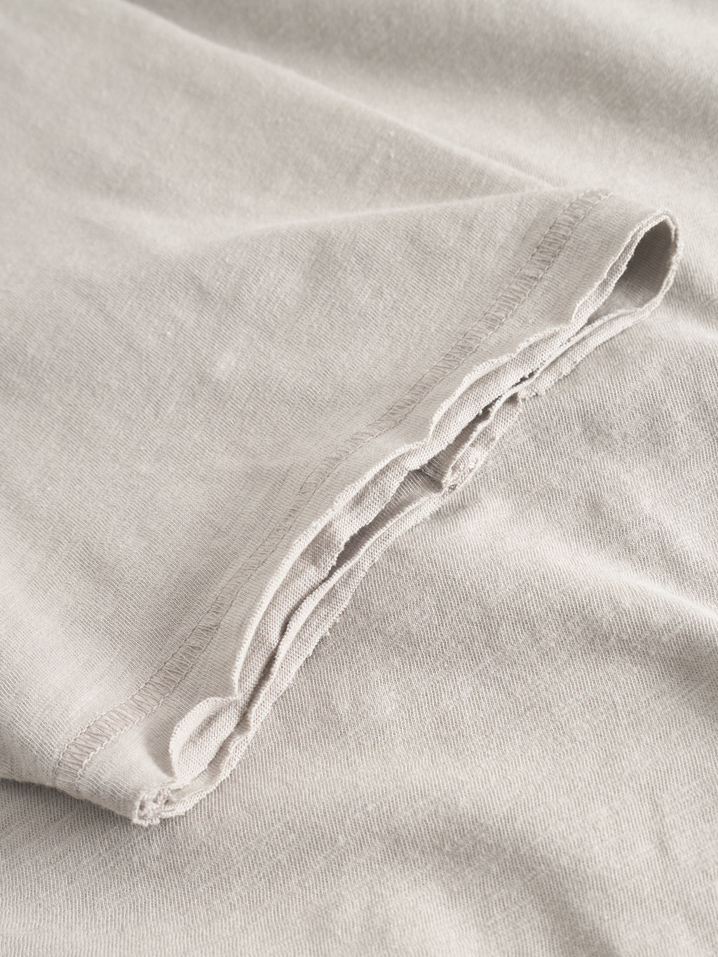 Close-up of Kostant New SS - Grey Paloma by Gabba, featuring light beige-grey slub fabric with a visible hem and flatlock stitch seam, highlighting the textured weave.