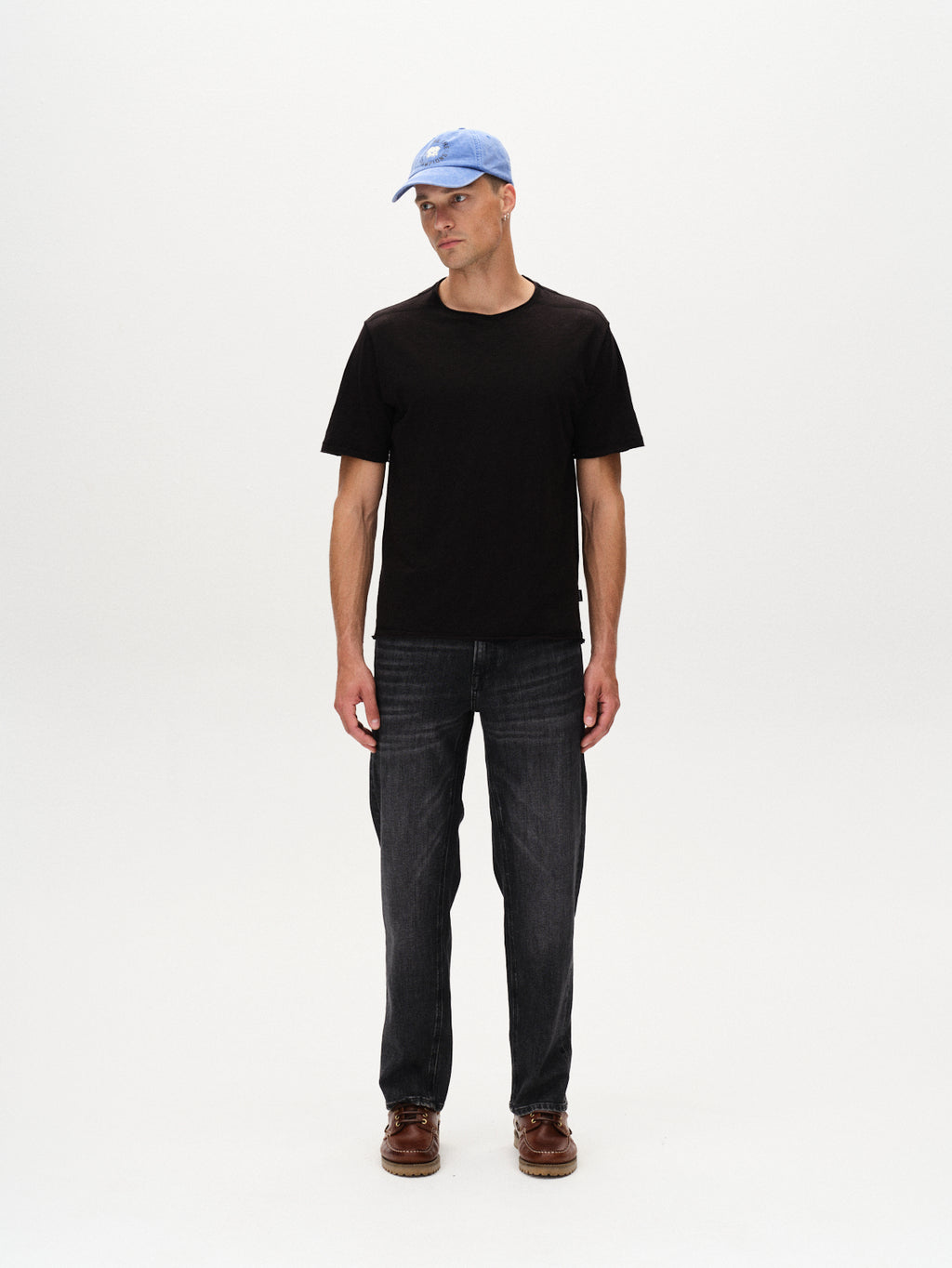 A man wears the Gabba Kostant New SS - Meteorite T-shirt in a relaxed fit, paired with dark jeans and brown shoes, standing against a plain white background with his arms by his sides, looking slightly to his left.