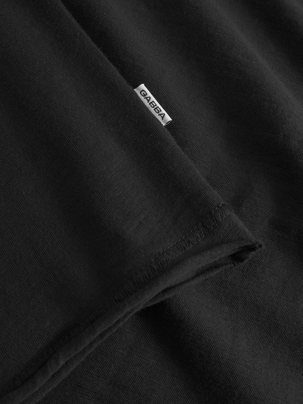 Close-up of the Kostant New SS - Meteorite T-shirt by Gabba, made from black slub fabric with a small white Gabba tag sewn into the seam. The soft, smooth material is ideal for a modern casual look.