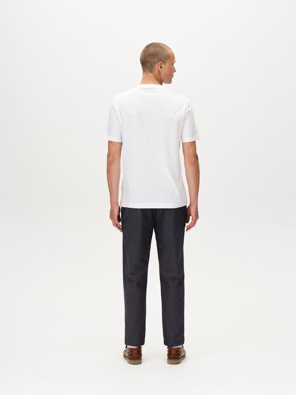 A man faces away from the camera, wearing Gabbas Monza Button Carre - Navy pants with an elastic waist and brown shoes, paired with a plain white T-shirt against a white background.