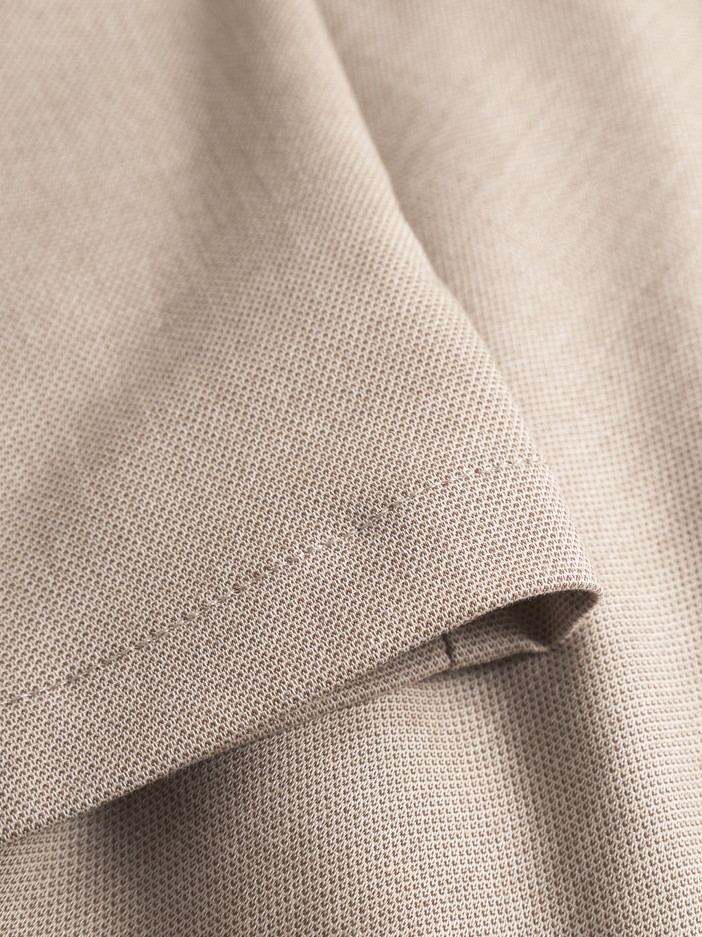 Close-up of the Monza Button Carre - Sand by Gabba, showcasing its beige textured fabric with visible stitching and a neatly folded corner. The lightweight woven material features a subtle pattern, reminiscent of relaxed straight pants with an elastic waist for comfort.
