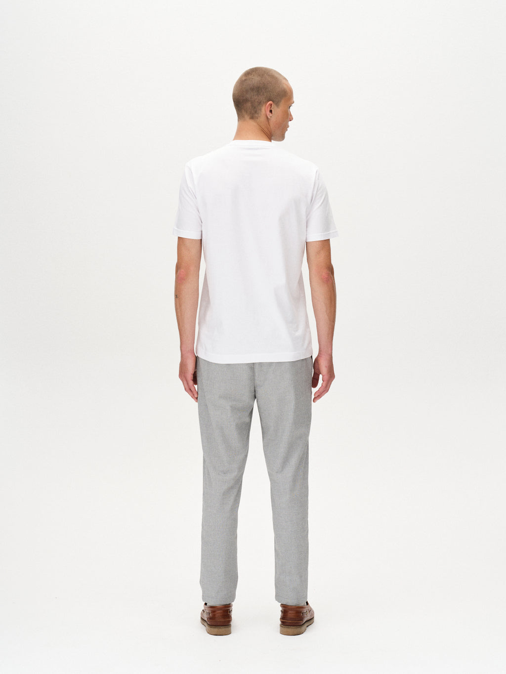 A man with short hair faces away from the camera, wearing the Gabba Monza Button Carre - Lt. Grey shirt and relaxed straight pants with brown shoes, styled against a white background for a versatile look.