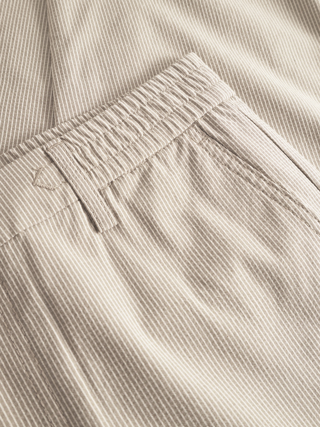 Close-up of Monza Button Com2 Cropped pants by Gabba in khaki, showcasing light beige and white pinstripes, an elastic waist, belt loop, and side pocket with detailed stitching for a classic silhouette.