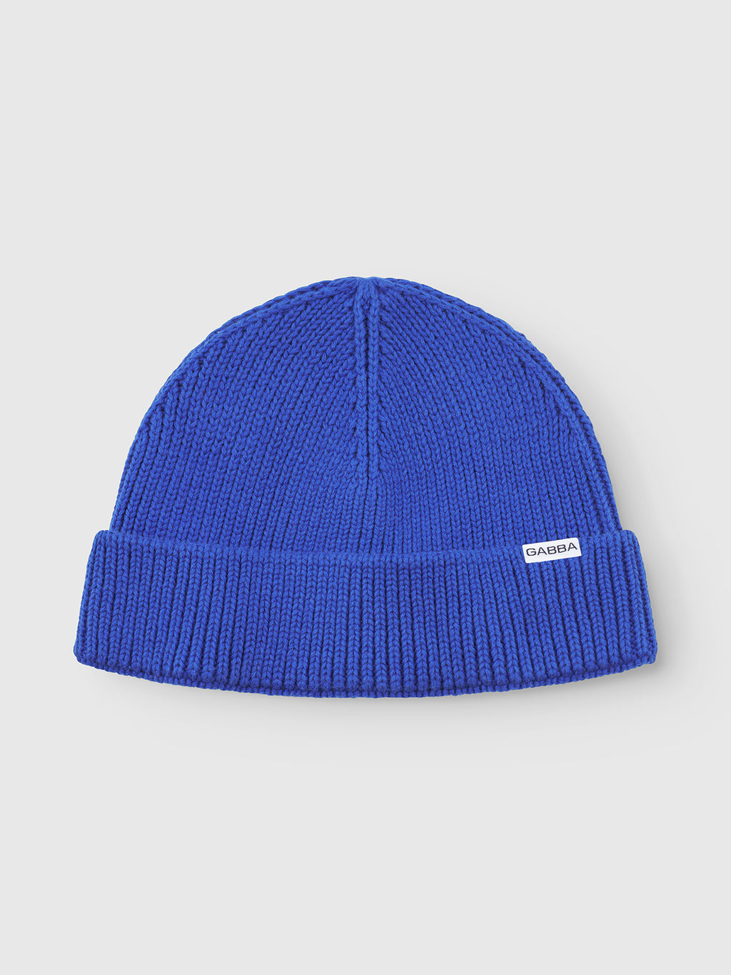 The New Mount Beanie - Blue by Gabba features a vibrant blue ribbed knit with a folded brim and a small white label at the front, strikingly set against a light background to emphasize its modern design.