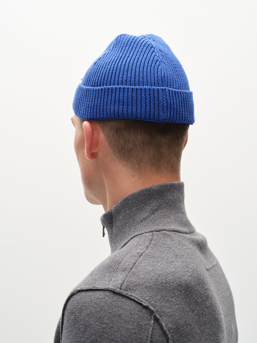 A person in a vibrant Gabba New Mount Beanie - Blue and a gray zip-up sweater stands with their back to the camera against a plain white background.