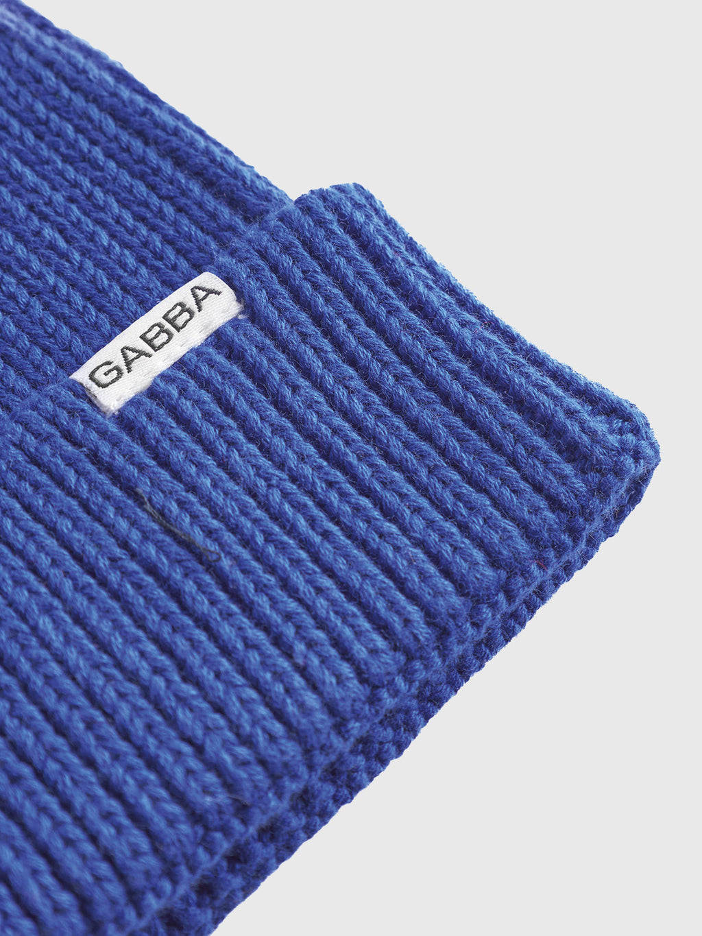 A vibrant blue New Mount Beanie by Gabba, featuring a white GABBA label on its folded edge, displays its ribbed knit pattern against a light background.