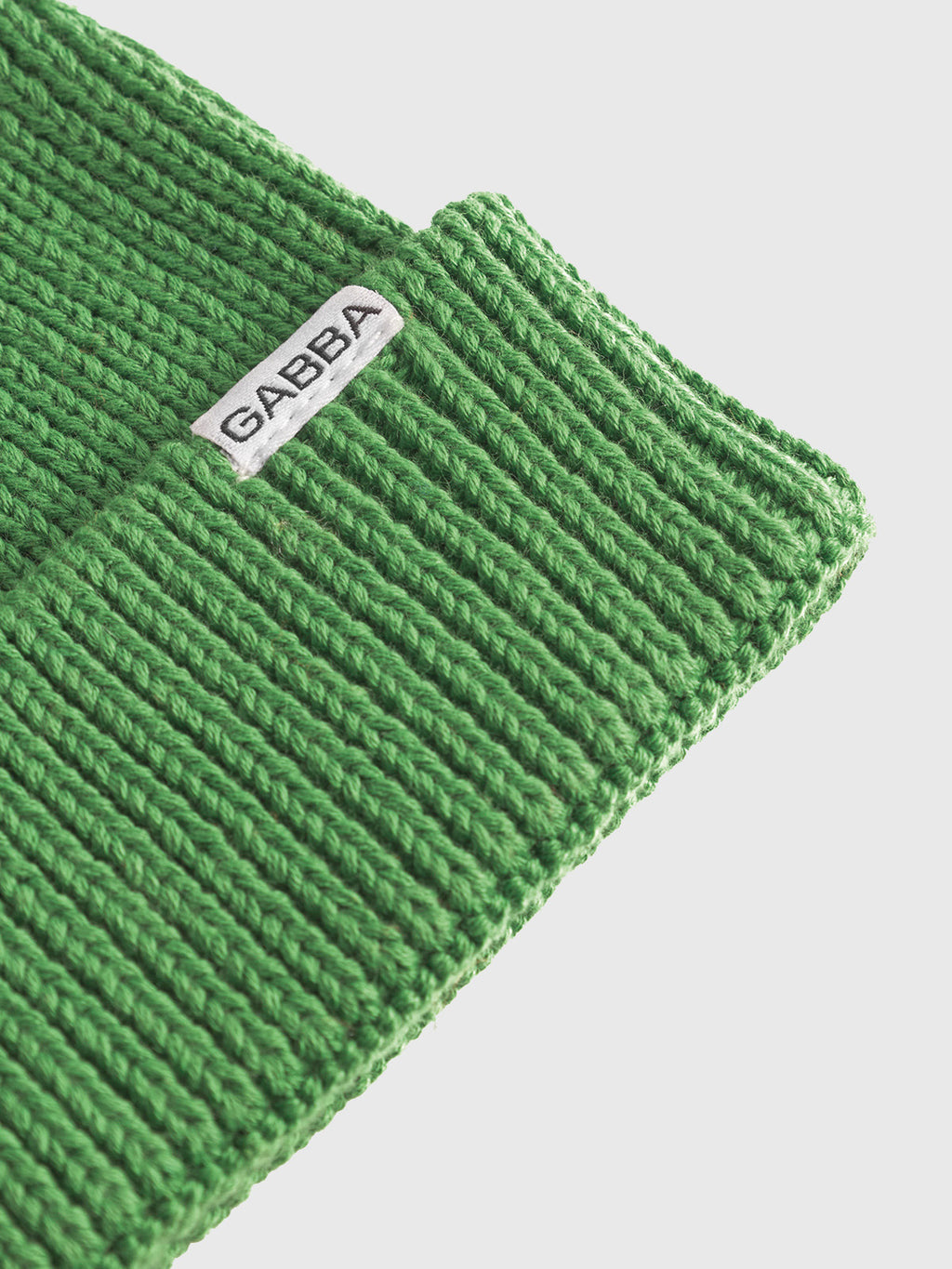 Close-up of vibrant green ribbed knit fabric labeled Gabba, likely part of the New Mount Beanie, set against a plain white background.