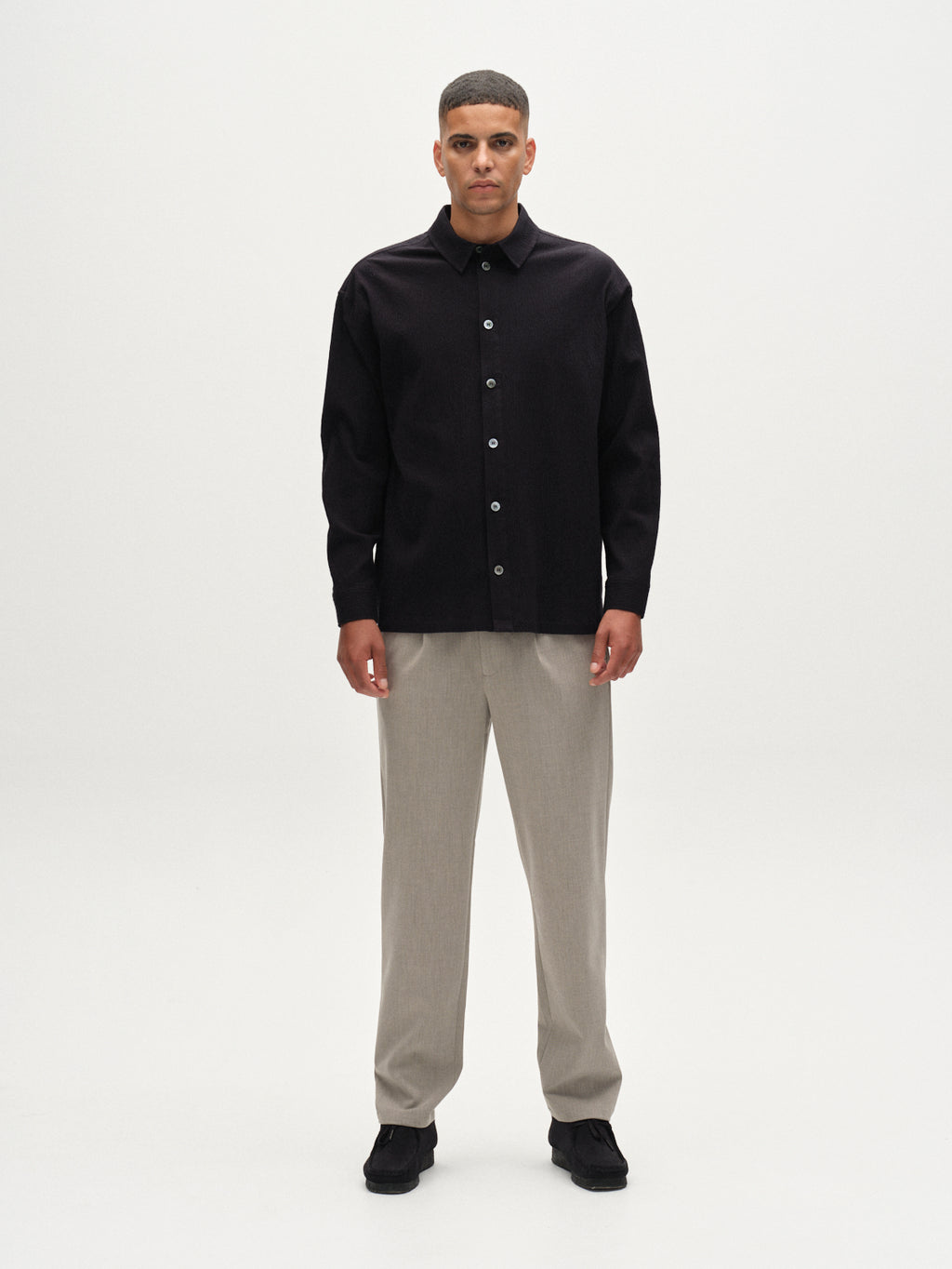 A man stands facing forward against a plain white background, wearing Gabba's GABnapoli 19 Phin GRS - Sand trousers. He pairs them with a black button-up shirt and black shoes, arms relaxed at his sides and expression neutral.