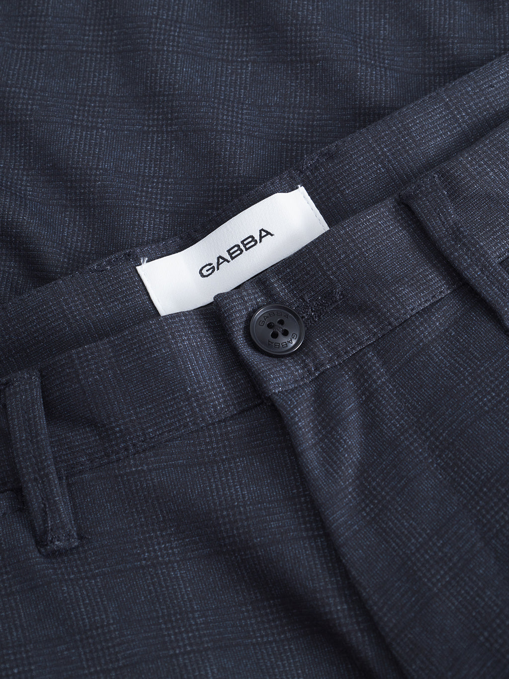 Close-up of GABpaul Nygo navy slim straight trousers by Gabba, featuring dark blue plaid pattern, black button, belt loops, and visible white Gabba label inside the waistband. Made from comfort-stretch fabric for tailored comfort.