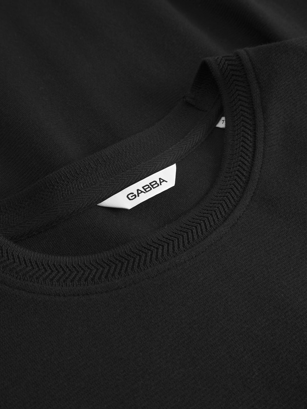 Close-up of the Dune Brush LS - Black by Gabba, a black crewneck long-sleeved tee featuring detailed collar stitching and a white label with Gabba in black letters—a must-have for the modern wardrobe.