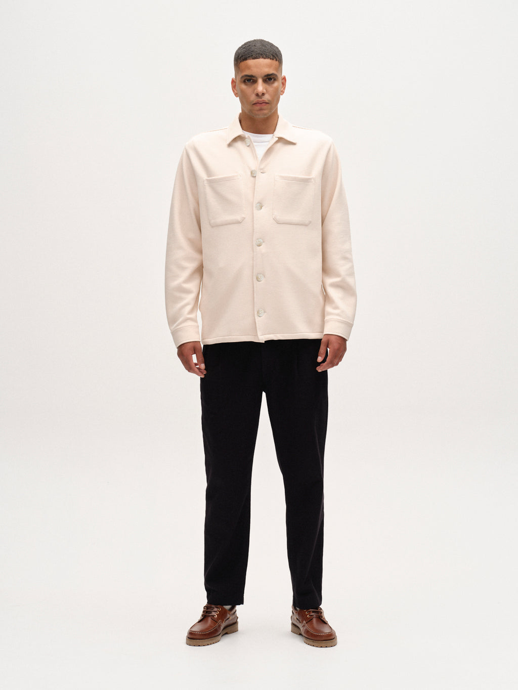 Man wearing a beige shirt and black pants on a white background