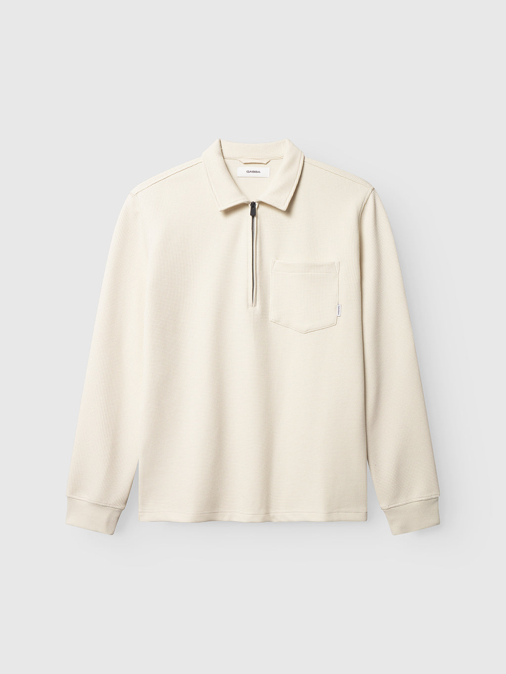 The Gabba Island Waff - White Almond is a cream-colored waffle knit shirt with long sleeves, a zippered collar, and chest pocket, showcased against a plain light gray background for a modern mens style.