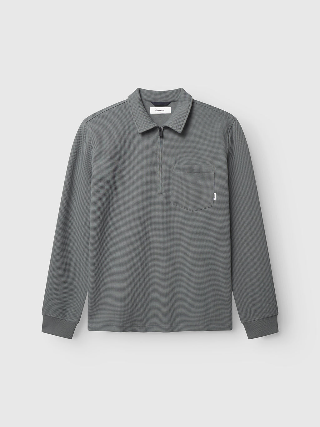 The Gabba Island Waff in Dust Sage Green is a long-sleeve collared pullover with a partial zipper, left chest pocket, ribbed cuffs, and a textured waffle finish, shown on a plain light background.