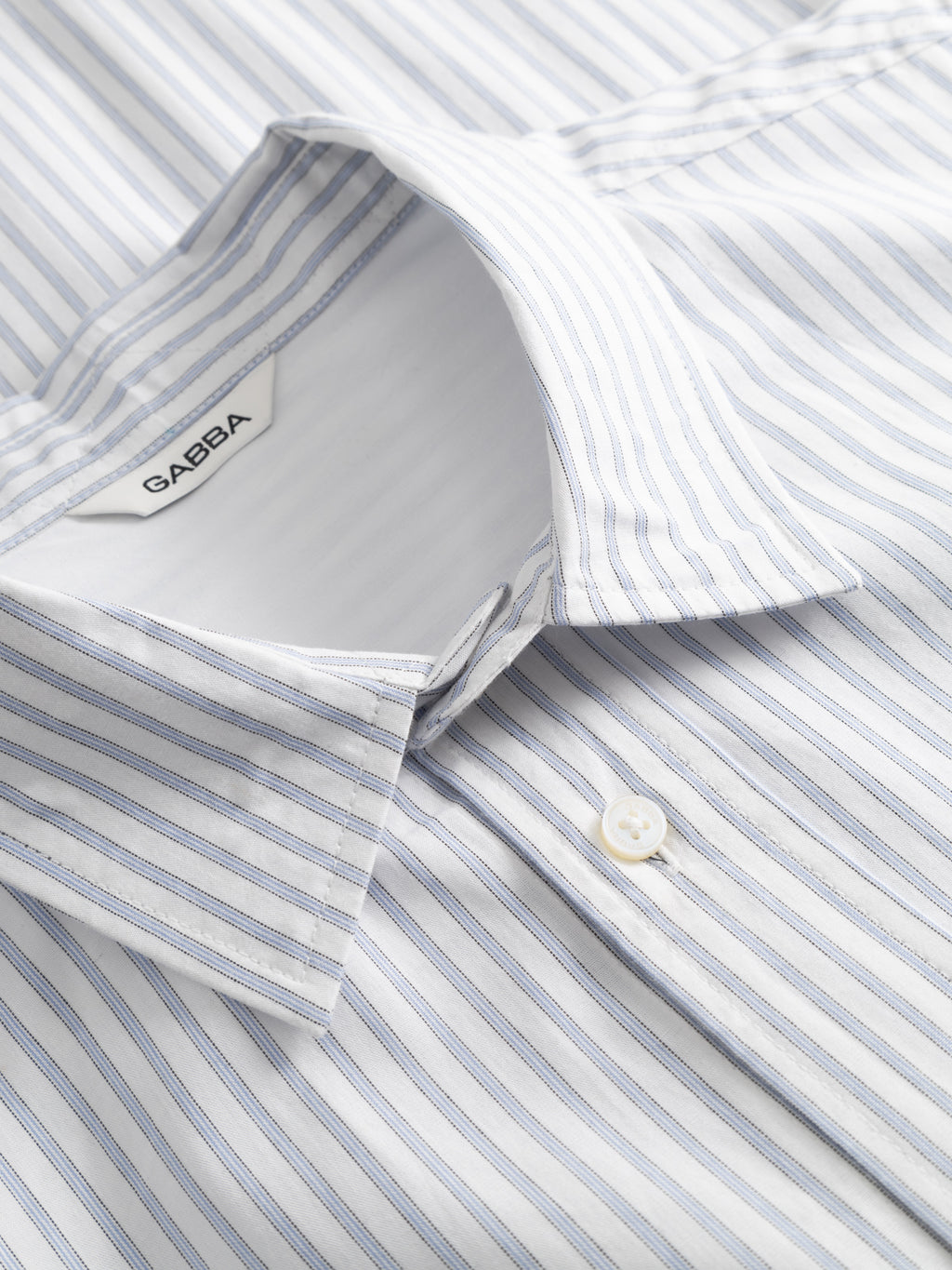 Close-up of the Gabba Sven Reg Clo Ls white stripe shirt with thin blue vertical lines, regular fit, pointed collar, single white button, and branded label inside the collar.