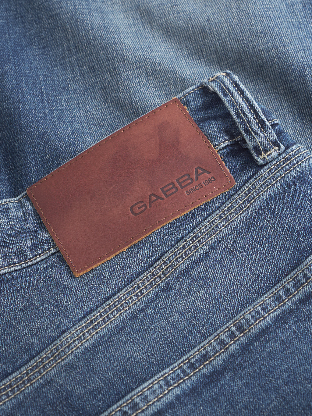 A close-up of Carl Jingo - Dark Blue Denim stretch jeans with a brown leather waistband patch embossed with Gabba and SINCE 1983.