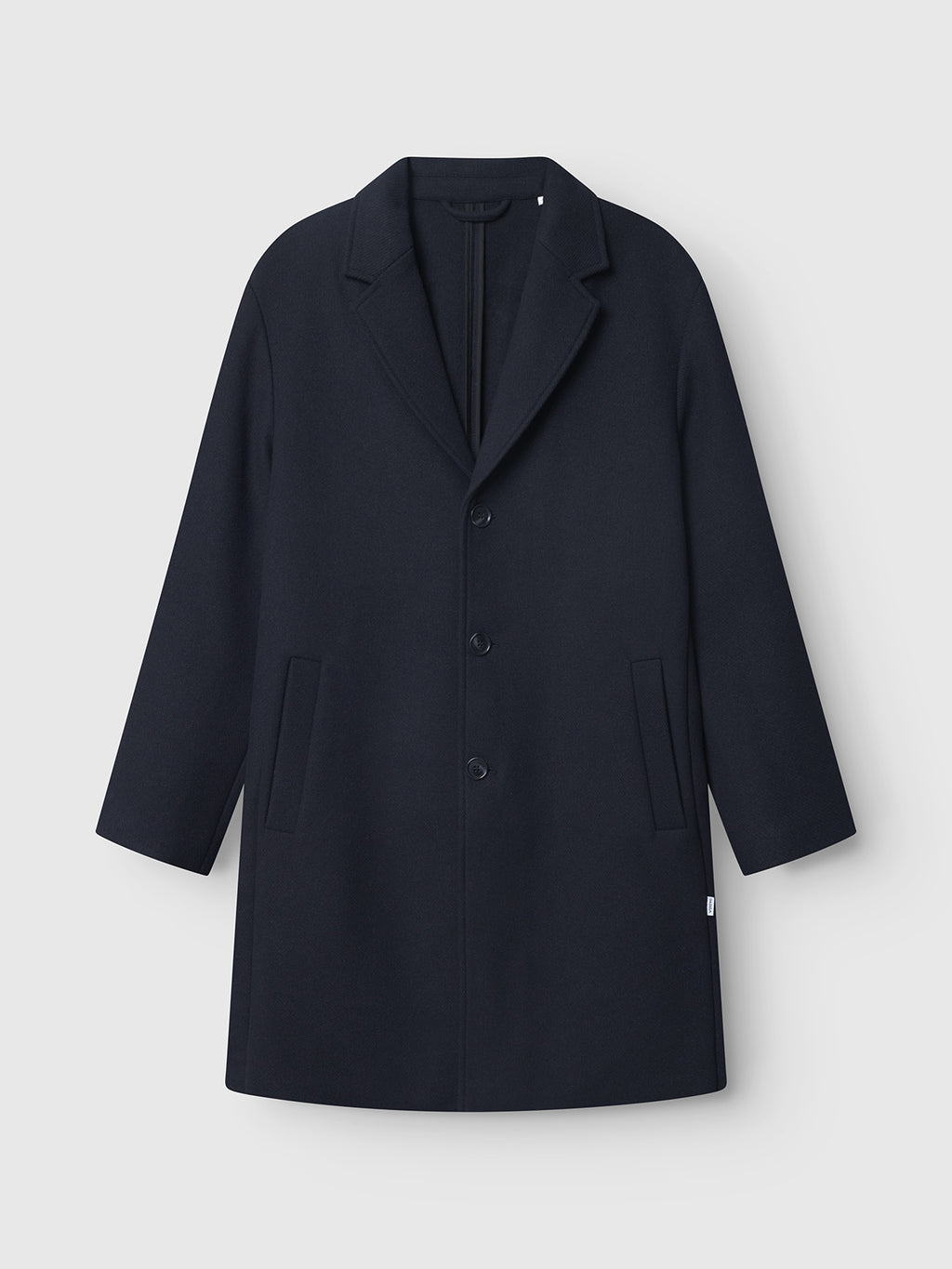 The Gabba Leeds Drift coat in navy is a knee-length, oversized wool design featuring a notched collar, three front buttons, and two slanted pockets, shown on a plain white background.