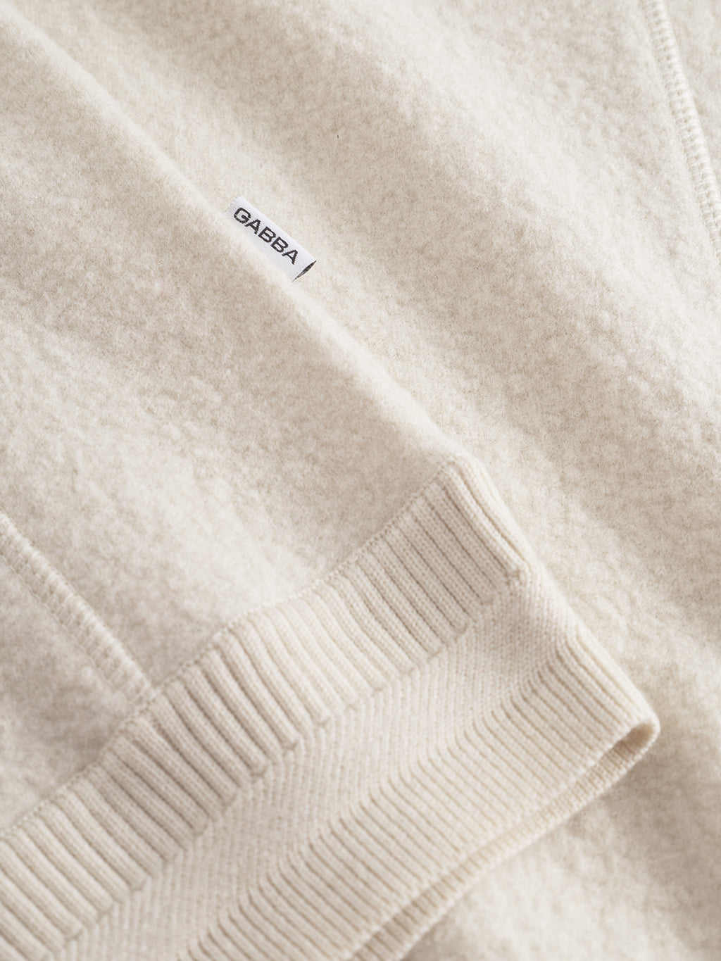 A close-up of the Gabba Bristol Led sweater in White Almond, featuring ribbed cuffs and a small white label with the Gabba logo.