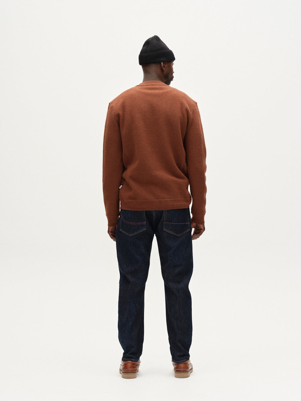 A man, seen from behind against a plain white background, wears Gabba's Bristol Led - Brownish textured wool sweater, dark blue jeans, brown shoes, and a black knit beanie.
