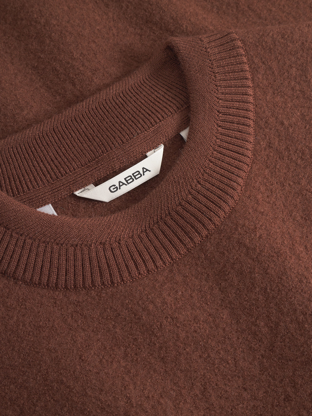 Close-up of a soft, brown-textured 'Bristol Led - Brownish' sweater with a ribbed crew neckline. A white label inside the collar displays the Gabba brand in black letters.
