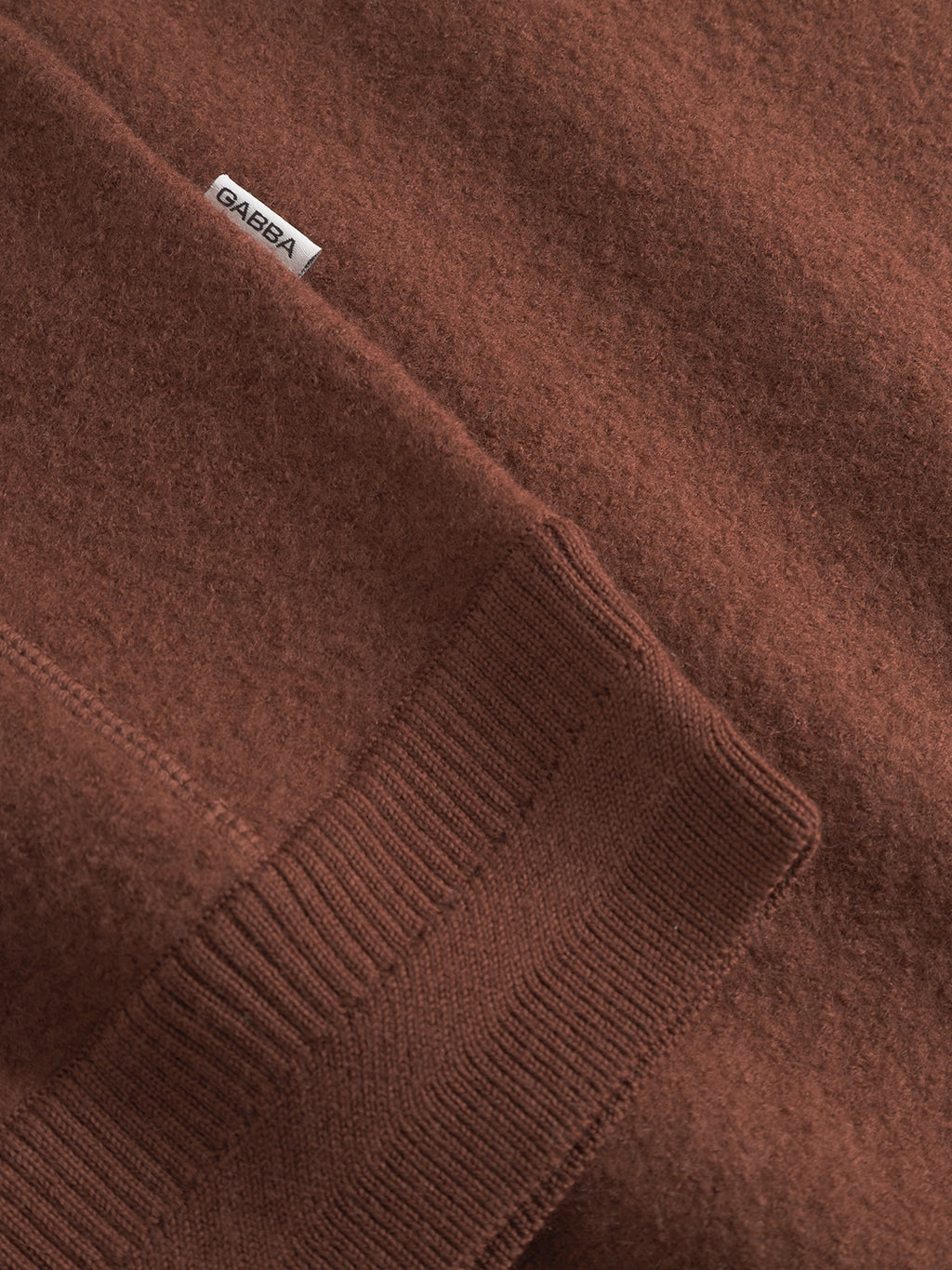 Close-up of a textured Bristol Led - Brownish wool sweater, featuring ribbed cuffs and a white Gabba label sewn near the seam.