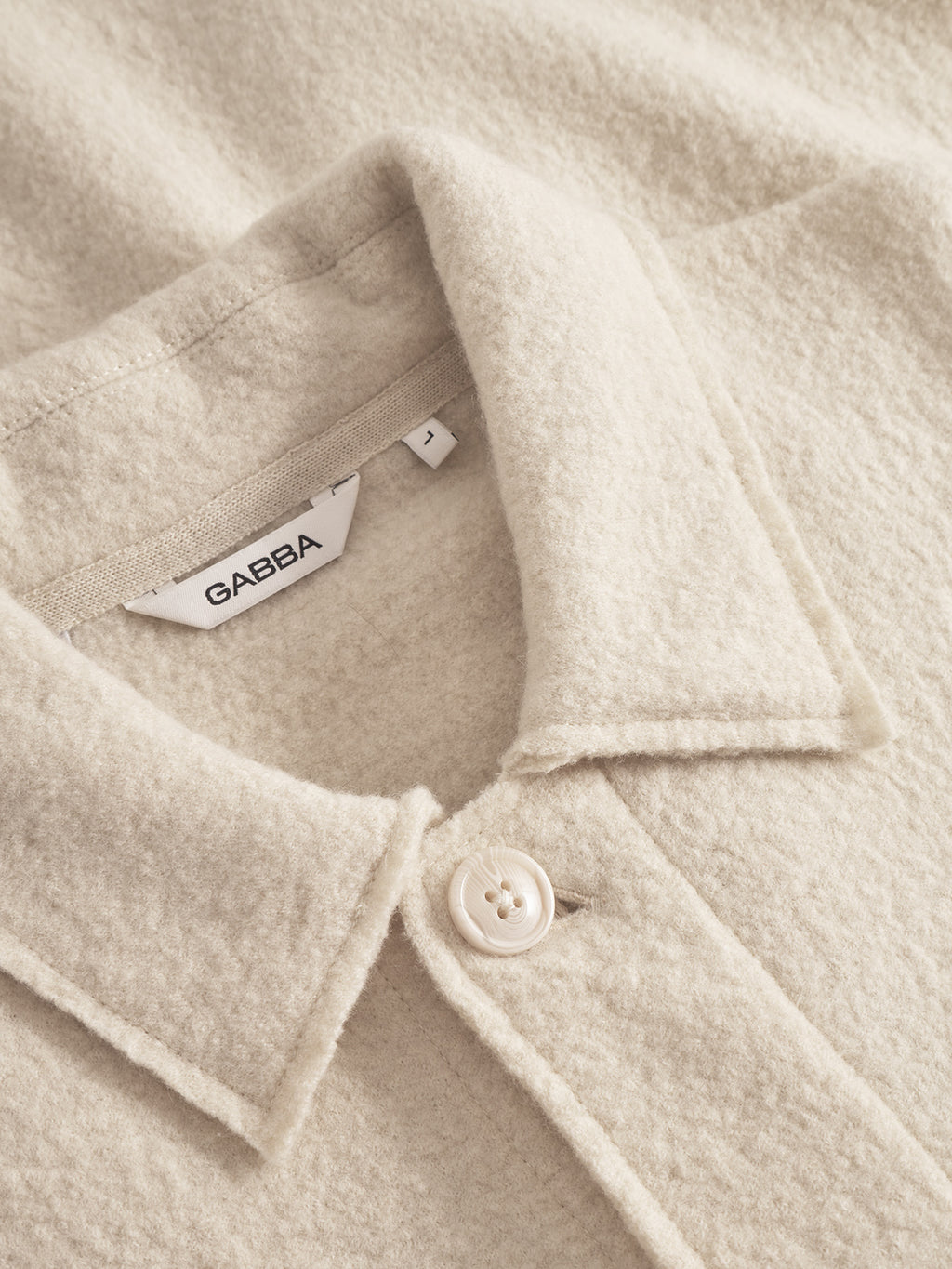 Close-up of the Preston Led - White Almond wool overshirt by Gabba, featuring a beige textured finish, collared design, single cream button, and visible white label with