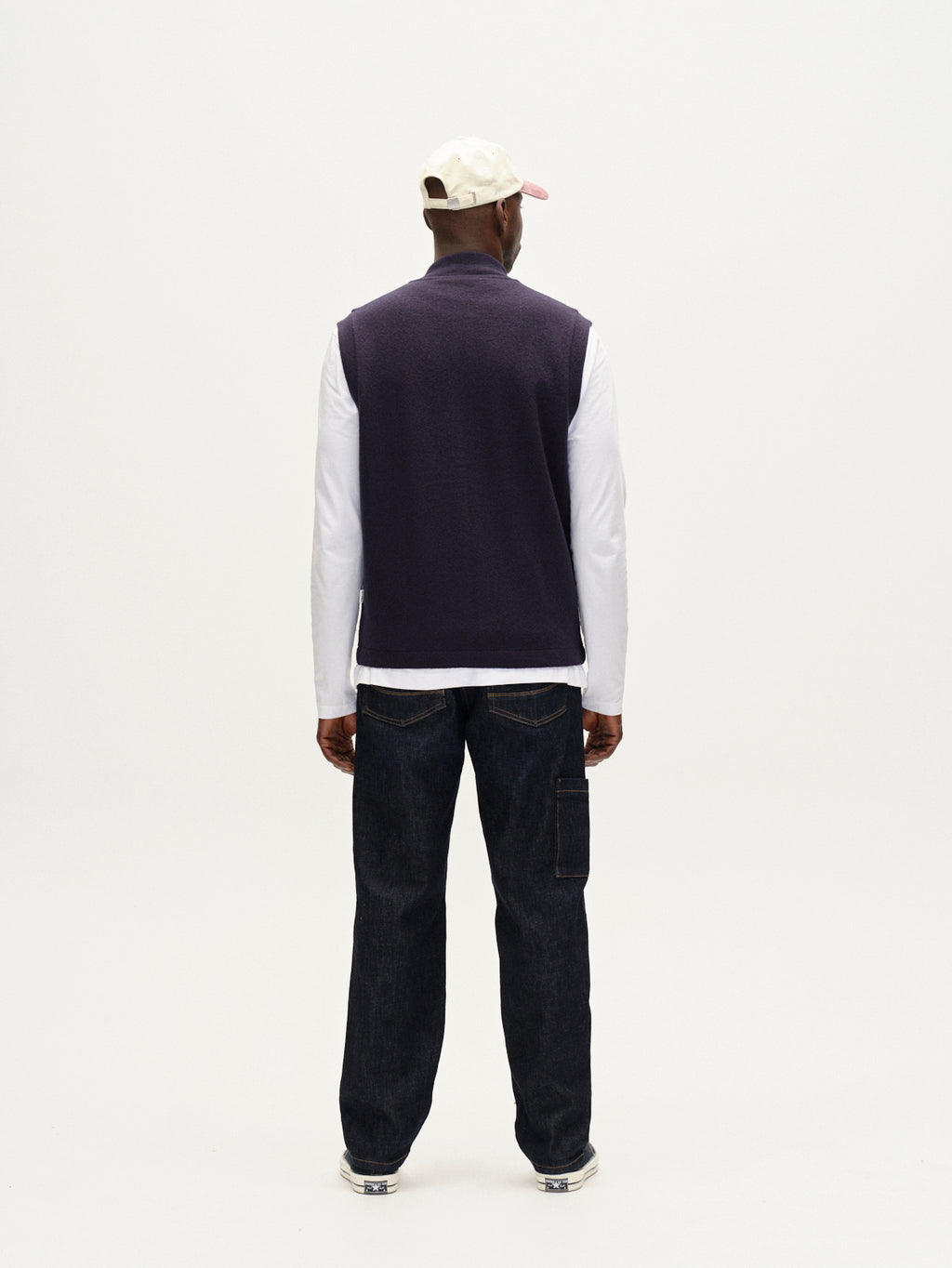 Someone wearing the Gabba Norwich Led - Navy utility vest over a white long-sleeve shirt, paired with dark jeans and a white cap, stands facing away against a plain white background.
