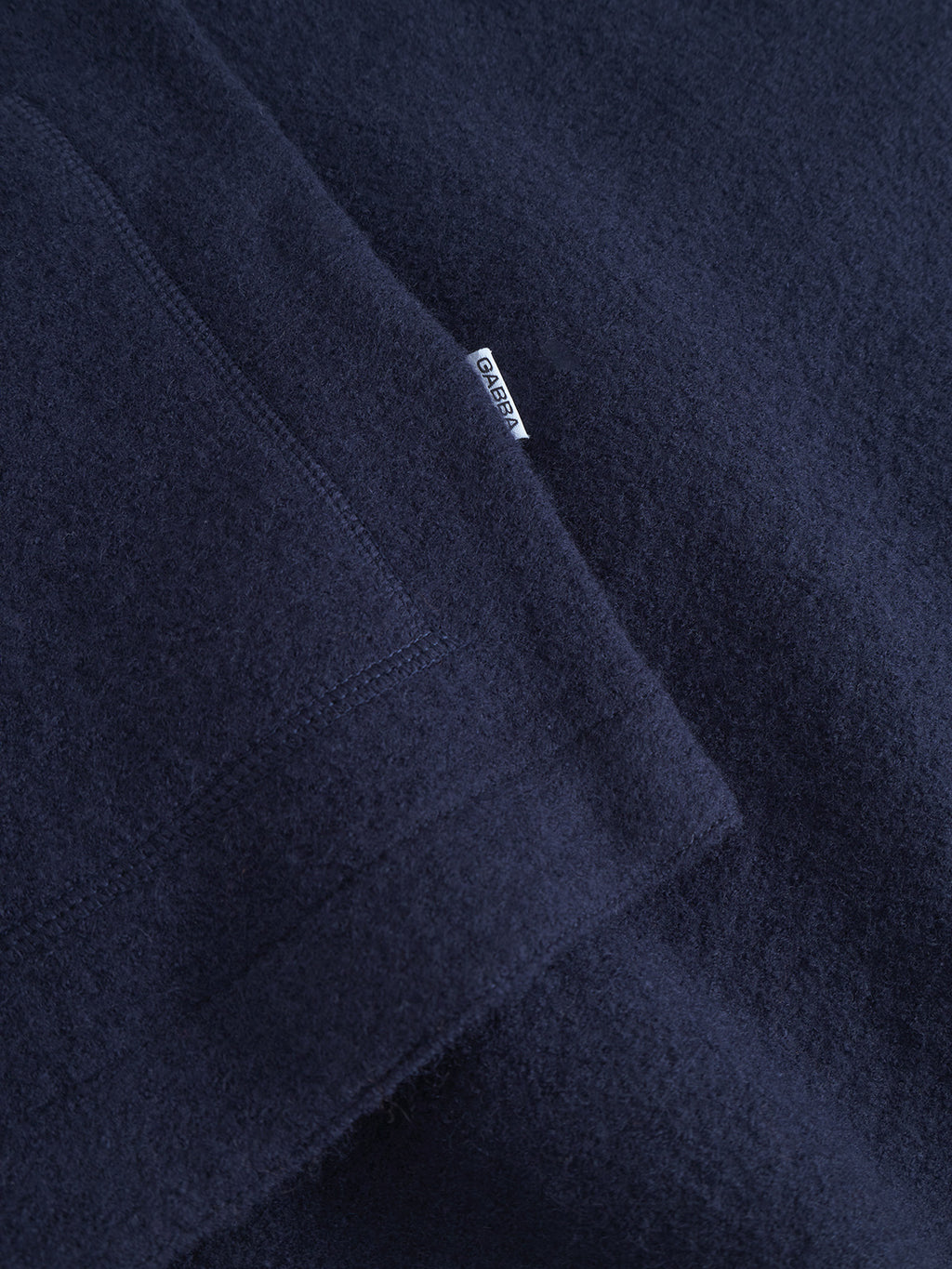 Close-up of Norwich Led - Navy by Gabba: dark navy blue wool fabric with visible texture and stitching, plus a small white tag. A perfect classic detail for a wool vest or essential layering piece.