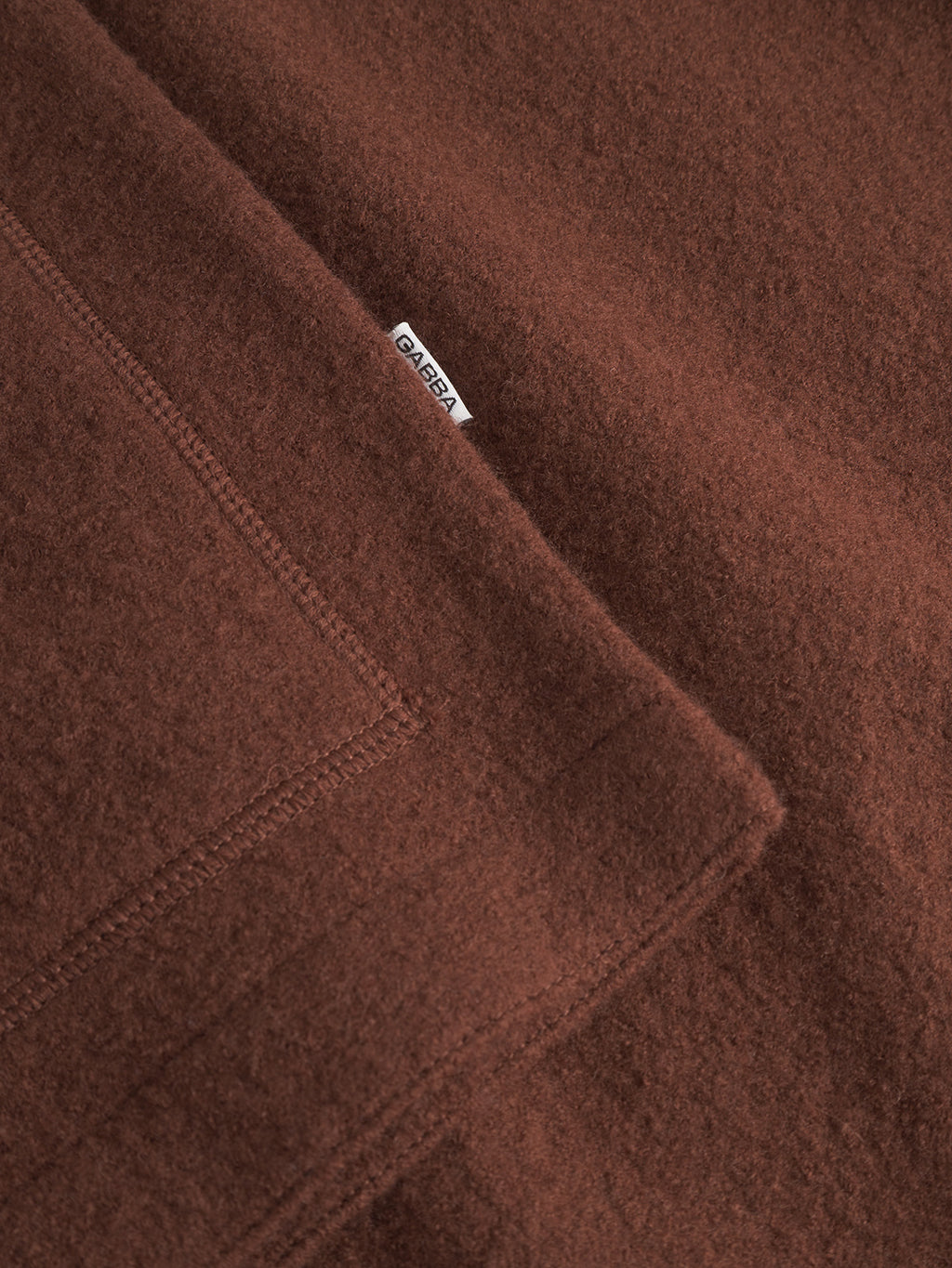 Close-up of Norwich Led - Brownish by Gabba: soft brown woolen fabric with visible stitching and a white Gabba label, partially tucked into the seam—ideal for cozy layering or as a stylish wool vest.