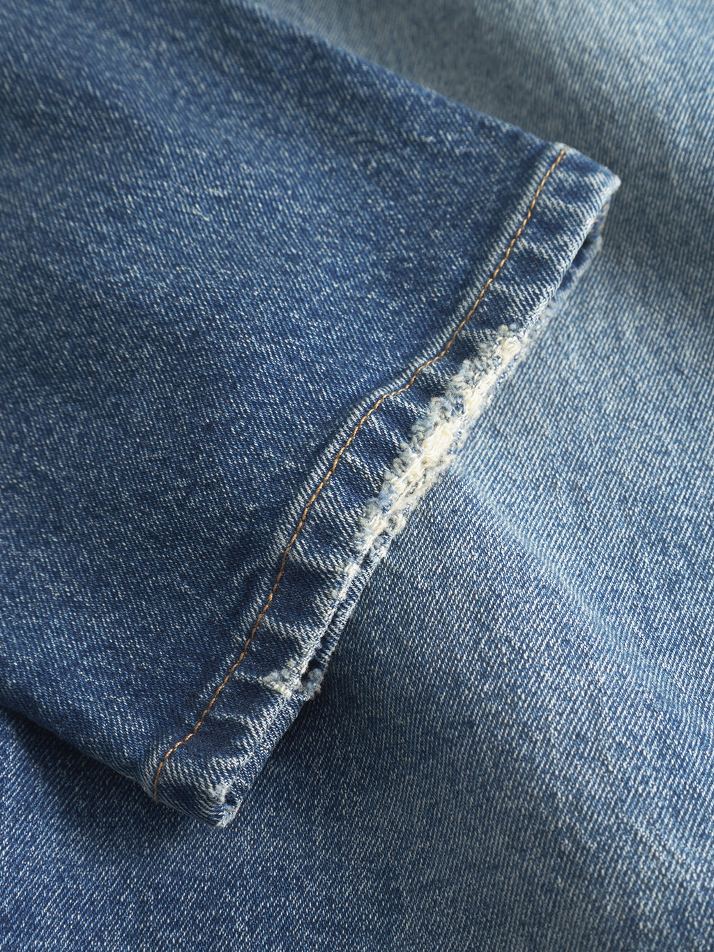 Close-up of folded Gabbas Carl Oskin Dark Blue Denim, showcasing visible stitching and a frayed edge. The texture and color variations enhance its casual style, with light and shadow highlighting its distinct look that complements a loose tapered fit.