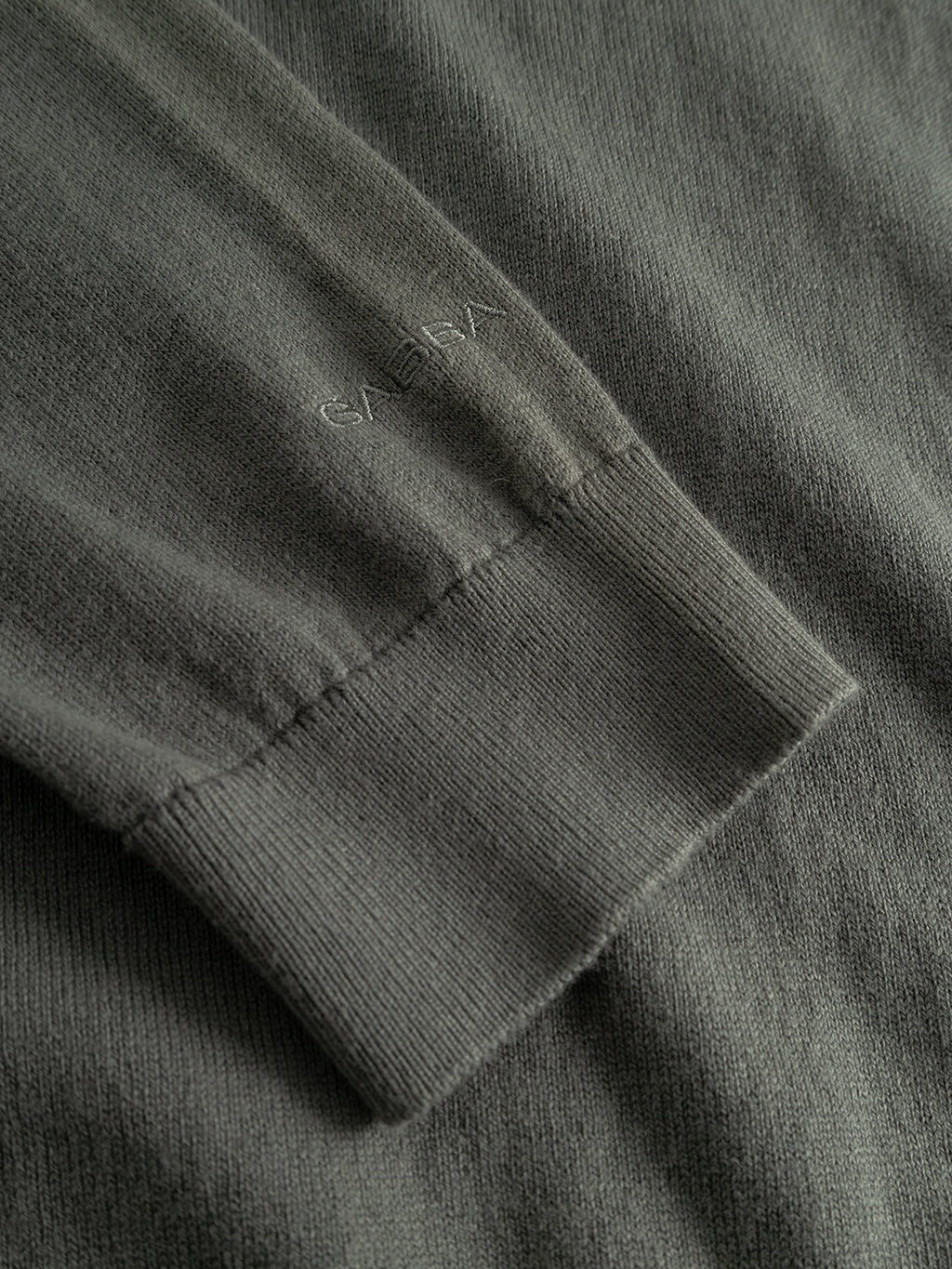 Close-up of the Gabba Akita Prex LS sweater sleeve in Dust Sage Green, featuring subtle “GAEMY” embroidery near the cuff and showcasing the fine cotton-cashmere texture and stitching.