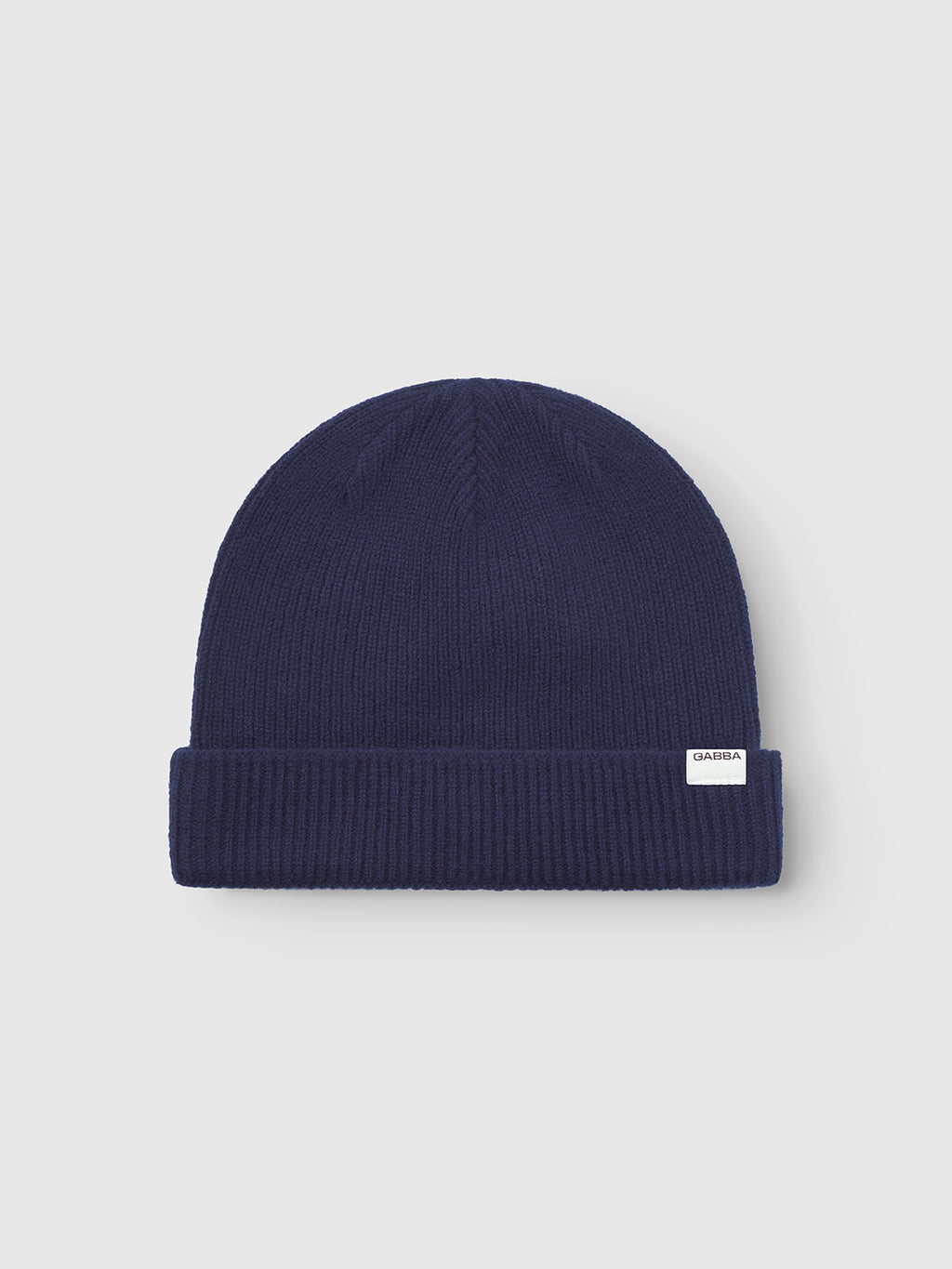 The Gabba Biella Aico - Navy is a soft merino wool beanie with a folded brim and a white rectangular label, shown on a plain light gray background—a perfect staple for cold weather.
