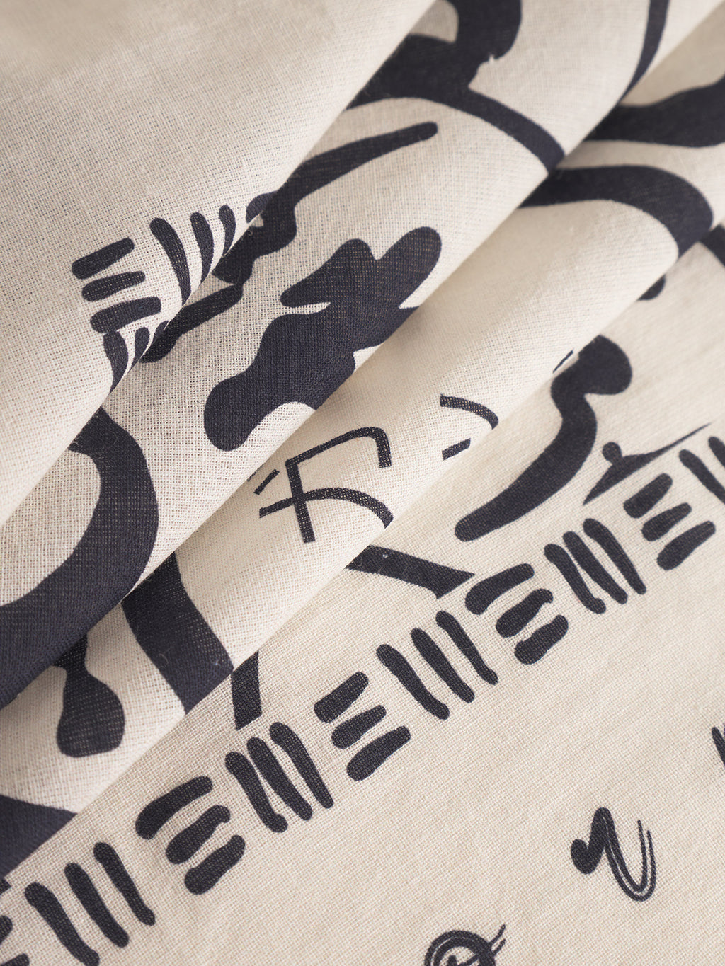 A close-up of the Gabba Bandana Yovi - Multi Pattern shows folded premium beige cotton with black abstract Japanese-inspired motifs for a layered, textured look—ideal for stylish wear.