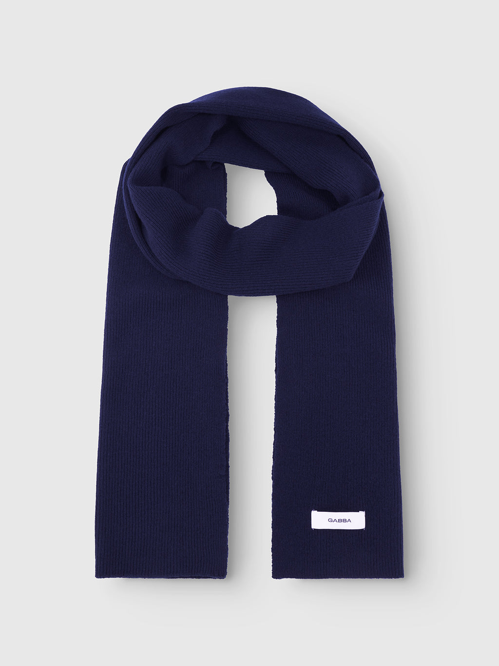 A navy blue ribbed knit scarf, the Biwa Aico - Navy by Gabba, is laid flat on a light gray background. A small white rectangular label near one end shows the brand name Gabba in black text.