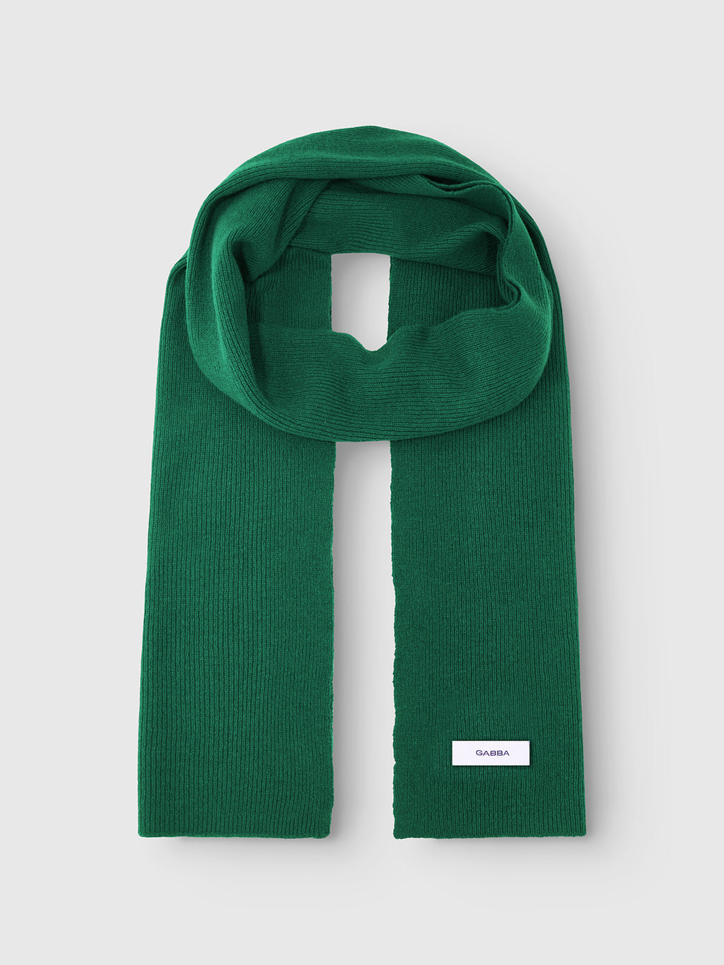 A green ribbed knit scarf, Biwa Aico by Gabba, is neatly folded with a small white label near the end on a plain light gray background.