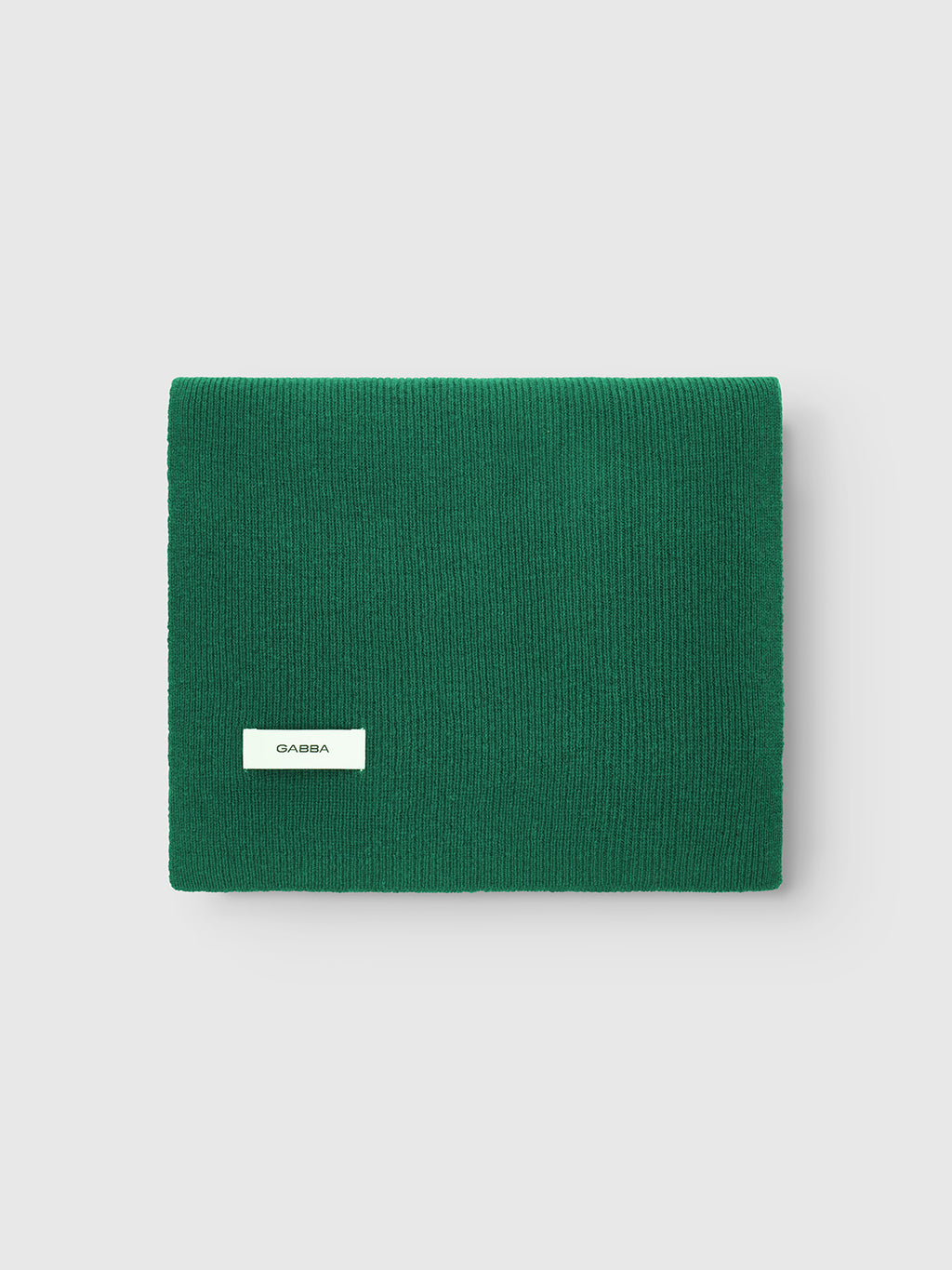 A neatly folded Biwa Aico - Green wool scarf from Gabba, featuring a small white Gabba label, rests on a plain light gray background.