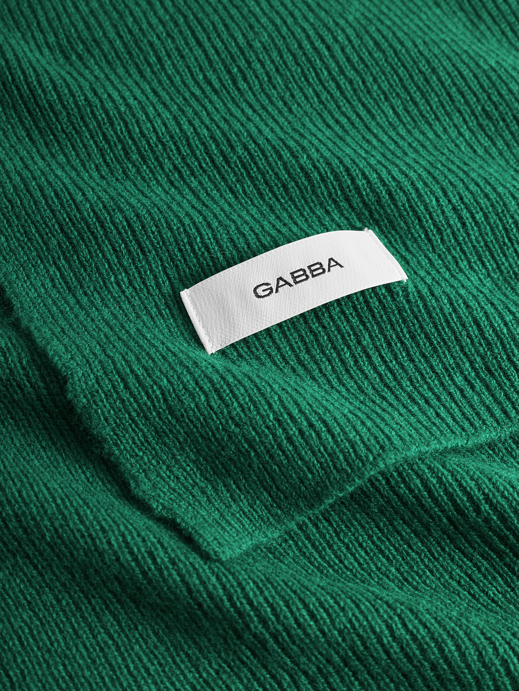 A close-up of the Biwa Aico - Green ribbed knit scarf highlights a white Gabba label sewn onto the soft material.