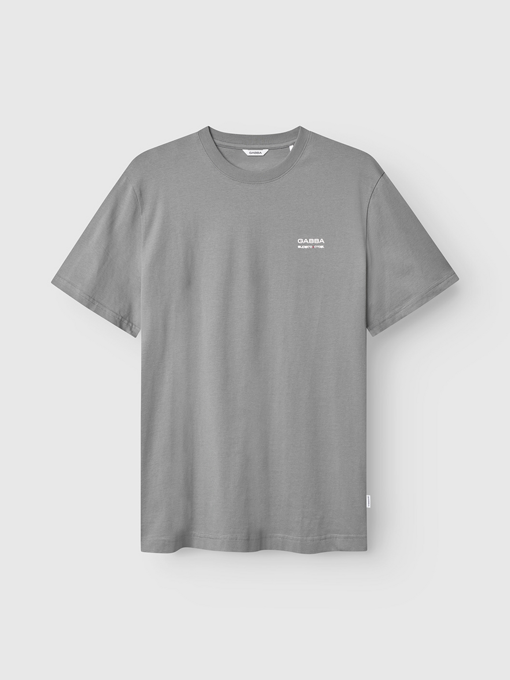 The Dune Kay Man Bauw SS GOTS in Dust Sage Green by Gabba is a minimalist T-shirt, featuring a small white Gabba logo and text on the left chest. Made from GOTS-certified organic cotton, it’s shown against a plain light background.