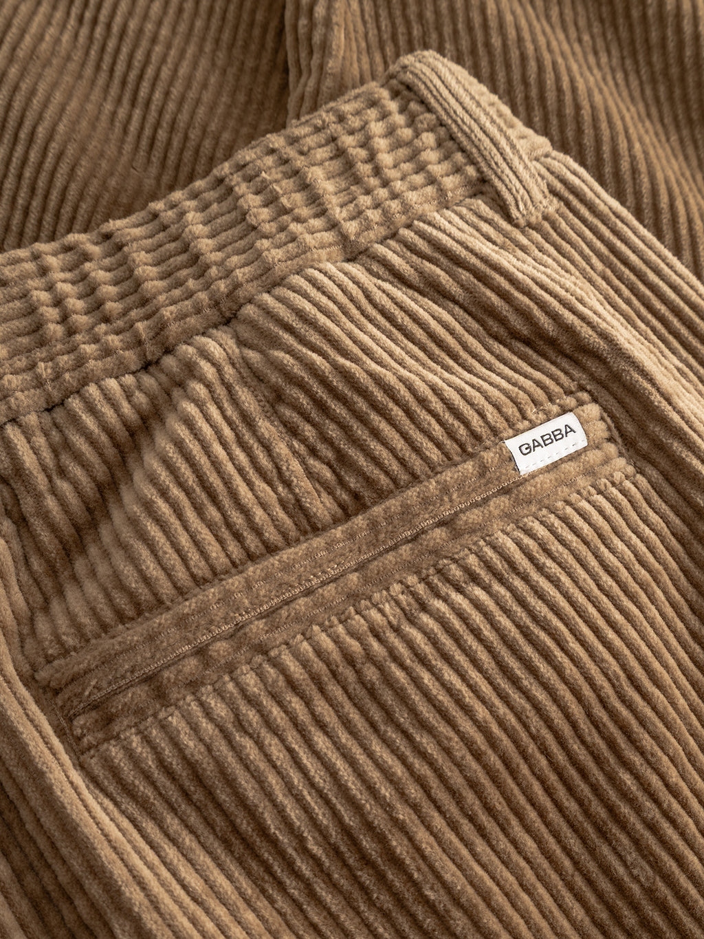 Close-up of the Monza Ibre - Sand corduroy trousers by Gabba, highlighting their textured comfort stretch fabric, back pocket, and a small white brand label above the pocket for added casual sophistication.