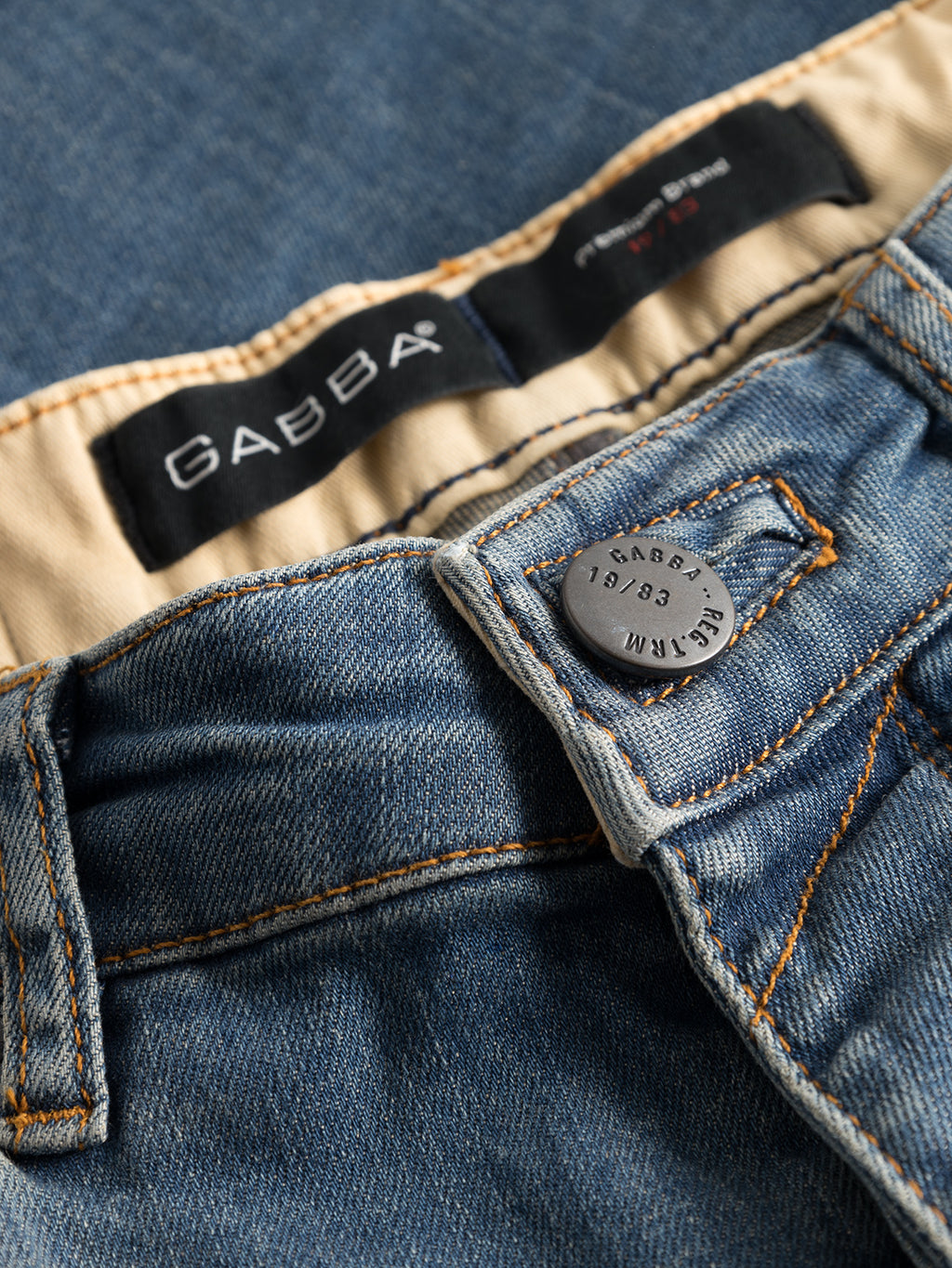 Close-up of Rey 44617 Jeans - Denim wash with a visible GABBA button. The inside waistband displays branded tags. These slim jeans feature blue fabric with orange stitching, capturing a laid-back look and classic jeans appearance.